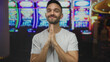 © Krakenimages.com - Young man in casino with slot machines in background showing praying gesture indoors showing anticipation and hope during casual play in gambling environment