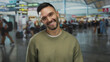 © Krakenimages.com - Young man smiling at airport terminal showing peace signs with a lively background, capturing the essence of travel and a vibrant atmosphere.