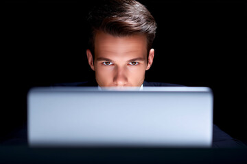 Focused man working on laptop screen in the dark, intense concentration in low-key lighting