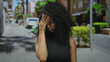 © Krakenimages.com - Young hispanic woman with curly hair and glasses stands on a vibrant street appearing thoughtful in an outdoor urban setting with blurred background.
