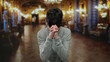 © Krakenimages.com - Young man praying in an ornate museum hall with blurred classical sculptures and golden lighting in the background, expressing deep contemplation and reflection.