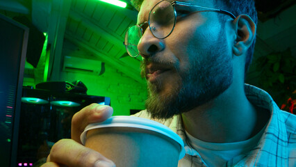 Pensive Caucasian man professional software engineer guy male coder programmer crypto specialist drinking coffee workplace looking computer thinking pondering creating innovative digital application