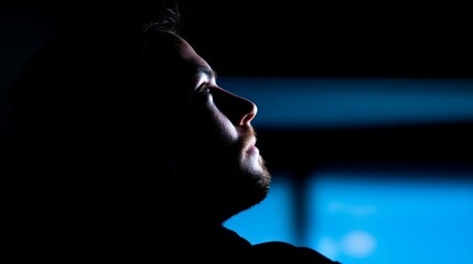 A male developer focused in a dark room, illuminated by the glow of a computer screen.
