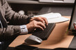 © nick_fedirko - Close-up of businessman in suit typing on wireless keyboard at modern office desk. Notebook, mouse, and smartphone visible on workspace.