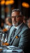 © PRASETIYO - A mature man in a grey suit sits at a table, gazing intently at the camera.  The setting appears upscale