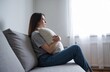 © Viktor - Pensive young woman hugs cushion, seated on couch at home, staring out window with sad thoughts. Reflects on breakup, feels lonely, frustrated, misses partner, experiencing solitude, deep melancholy.