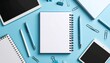 © Rupa - Overhead view of a workspace setup with notebooks, pens, and tablets, arranged on a blue surface.