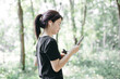 © tai - Young woman using smartphone in a lush green forest