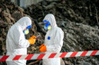 © BESTIMAGE - Two scientists in full protective hazmat suits working outdoors with laboratory tools near rocky terrain and caution tape, conducting environmental or hazardous material testing