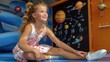 © Diffin - A young girl in a floral dress sits on the floor, smiling, with a space-themed board and model planets in the background.