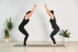© TRAVELARIUM - Two adult women practice yoga together in minimalist room. Dressed in black activewear, they are positioned on yoga mat, engaging in focused physical exercise