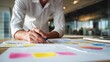 © mangolovemom - A person in a white shirt is working on colorful charts and graphs, analyzing data for a business or project in a modern office environment.