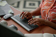© Seventyfour - Black woman typing on wireless keyboard at desk, hands visible with rings, working near laptop, smartphone, notebook and baseball, suggesting multitasking in modern workspace