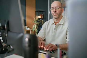 portrait of middle aged caucasian man wearing glasses working at computer in modern office, typing o