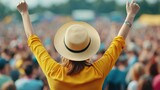 Young woman wearing a straw hat and a yellow shirt raising her arms and enjoying live music at a crowded festival