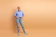 © deagreez - Confident mature woman in blue striped shirt and jeans standing relaxed against a beige background with a warm smile