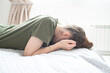 © Ruslan Russland - A tired young woman or teenage girl lies on a bed with her head down, covering her face with her hands.