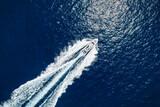 High aerial top view of a luxury yacht cruising with high speed over blue ocean leaving a trail of bubbles and waves behind