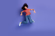 © deagreez - Excited young girl jumping in mid-air against a solid purple background wearing trendy casual t-shirt and jeans
