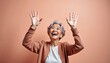 © yuntunen - Elderly woman smiling and raising hands against peach background