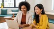 © MDJAMAL - Two smiling women of diverse ethnicity collaborate on a laptop in a modern office setting