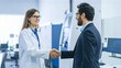 © photostockatinat - Two professionals in a laboratory shaking hands, signifying collaboration and partnership. A woman in a lab coat shakes hands with a man wearing a suit