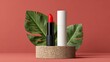 © Asayamrad - A vibrant red lipstick and its white case stand on a round stone platform, framed by two large green tropical leaves against a coral background.