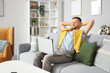 © Pixel-Shot - Young bearded man with laptop resting on sofa at home