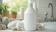 © agil - White plastic bottle of laundry detergent sits on a counter amongst soft towels and bath items near a window.