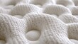 © AW - Close-up view of a mattress's textured surface.  A  soft, white,  knitted material with  raised,  rounded  bumps  and  small  holes