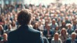 © AspctStyle - Confident male speaker addressing a large, attentive audience in a packed conference hall, viewed from behind the stage, with hundreds of seated attendees engaged in a professional seminar