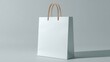 © Fenny - A pristine white paper shopping bag with light brown rope handles stands on a neutral gray background