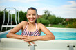 © bondarillia - Teen girl enjoying a summer day by the pool with a cheerful smile and relaxed demeanor in a sunny outdoor setting
