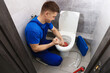 © New Africa - Plumber unclogging toilet with hand plunger indoors