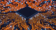 © rehan - Close up of a dark square chip surrounded by orange circuit board patterns and blue light effects