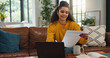 © peopleimages.com - Home, reading and woman with paperwork, financial planning and checking info with laptop and budget. Asset management, online and person with documents in living room, bills and analysis in house