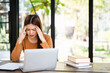 © Fahng - A woman is sitting at a desk with a laptop computer or notebook. She is looking at the laptop screen and she is in a state of stress or frustration.