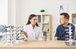 © Studio Romantic - Young man patient choosing glasses at optician store or in clinic with the help of friendly female doctor ophthalmologist consultation. Vision correction and ophthalmology concept.
