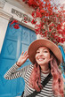 © EdNurg - Young woman tourist wearing hat in front of a traditional blue door and red flowers during summer vacation