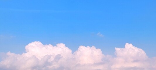 Wall Mural - Wide view of blue sky with fluffy white clouds on a sunny day with peaceful spring ambiance background. Soft white clouds float in the clear blue sky. Clear blue sky, bright spring.