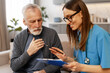 © Maria Vitkovska - Female doctor visiting elderly man at home taking notes on clipboard