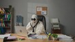 © kinomaster - Halloween businessman ghost in white sheet sits at office desk works on laptop wearing headset and talking with clients. Happy halloween business concept.