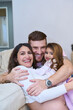 © Oscar - Happy latin family hugging on sofa, pregnant mother, father, and daughter embracing