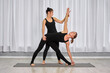 © TRAVELARIUM - Two adult women practice yoga in bright studio. One assists other in triangle pose. Peaceful atmosphere enhances concentration and balance