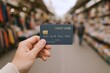 © Generative AI - Hand holding credit card with blurred supermarket aisle background, shopping and payment concept.