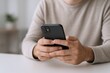© Generative AI - Close-up of a person holding a black smartphone in hand at home with blurred background.