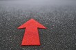 © Generative AI - Close-up of a red arrow on dark asphalt pointing forward for direction and guidance.