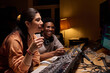 © pressmaster - Young adult Hispanic woman and young adult Black man working together at audio mixing console in recording studio, both smiling and focusing on computer monitor during music production