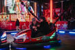 © qunica.com - A group of friends have fun driving bumper cars at a festive winter amusement park. The image captures joy, excitement, and the holiday spirit through colorful lights and cheerful expressions.