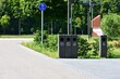 © Karolina - Modern waste sorting bins along city sidewalk near park. Eco-friendly recycling station encourages sustainability and clean public spaces. Clear labels guide proper waste disposal.